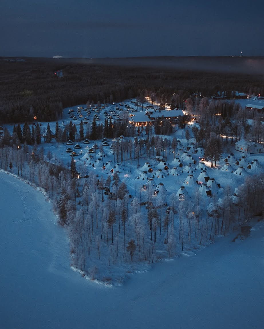 Aerial twilight view of illuminated aurora cabins at Apukka Resort beside a frozen lake near Rovaniemi