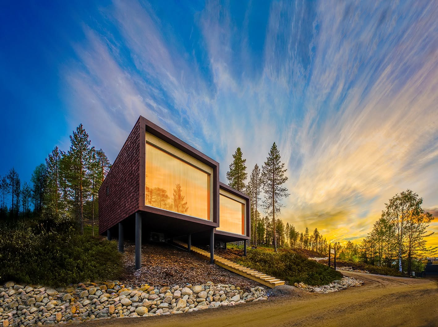 Modern timber cabins on stilts with large picture windows at Arctic TreeHouse Hotel in Rovaniemi at sunset