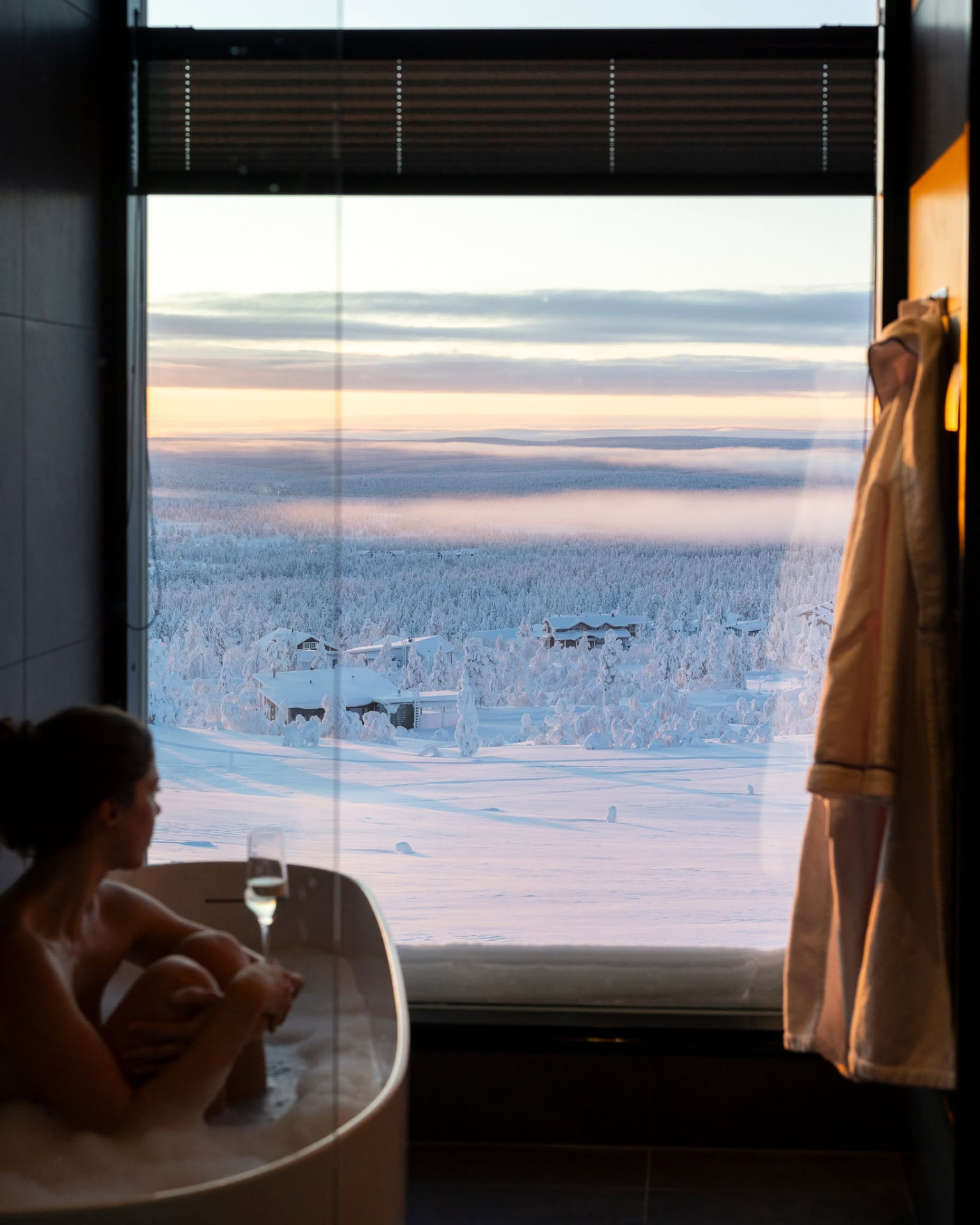 Hotel suite at Star Arctic Hotel in Saariselkä with a bathtub beside a picture window over snow-covered cabins and fells