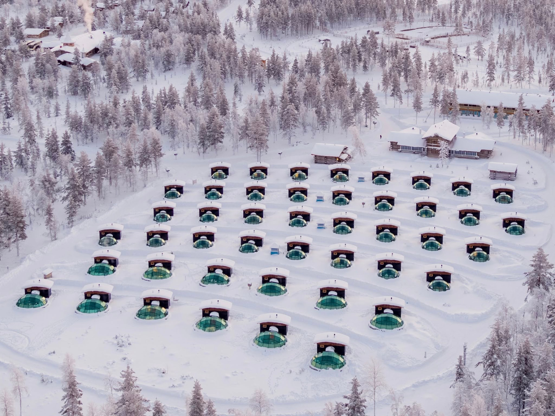 Aerial view of rows of glass igloo domes at Kakslauttanen Arctic Resort in a snow-covered clearing at Saariselkä