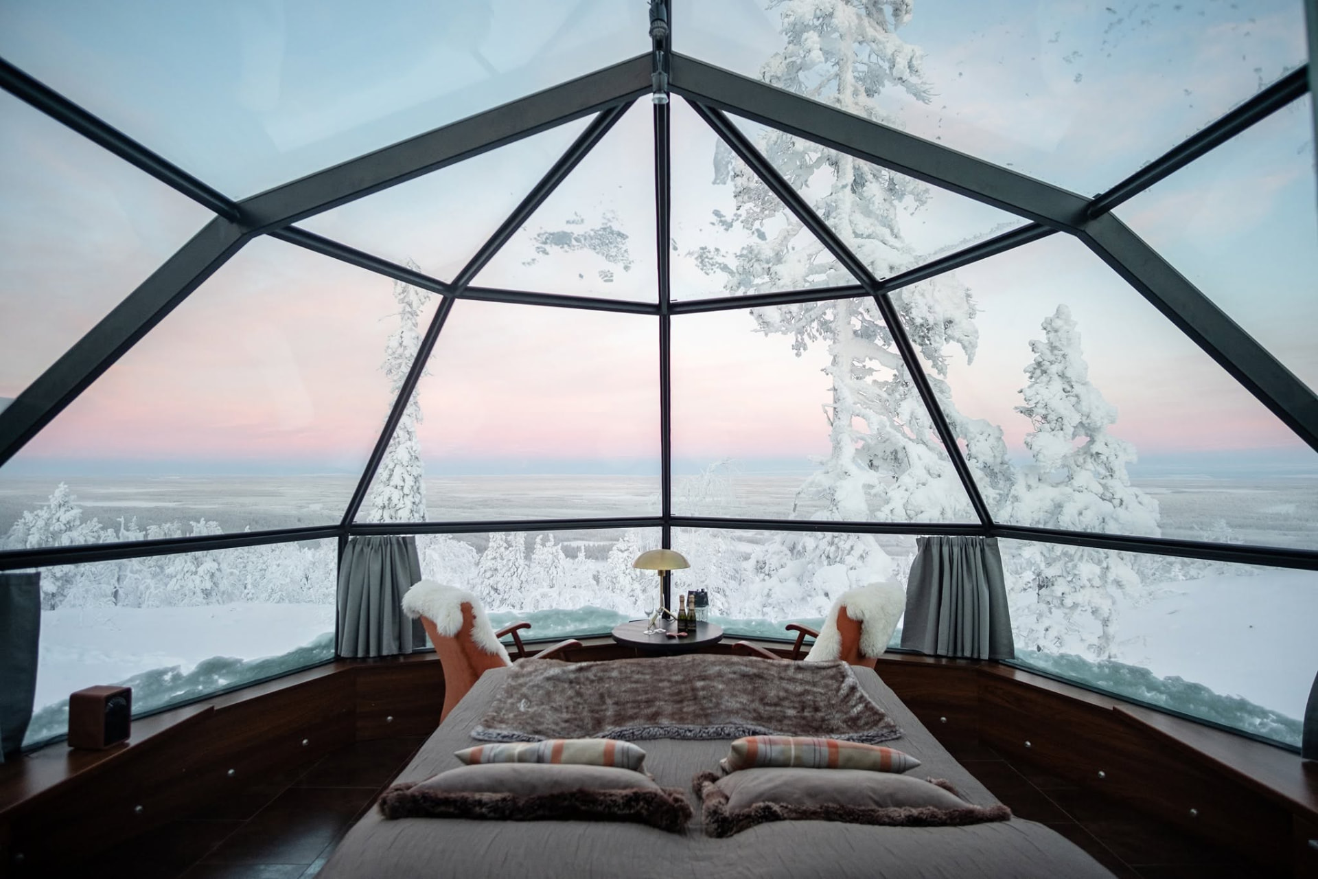 Glass-domed igloo bedroom at Levin Iglut looking out over snow-laden trees and the arctic plain near Levi